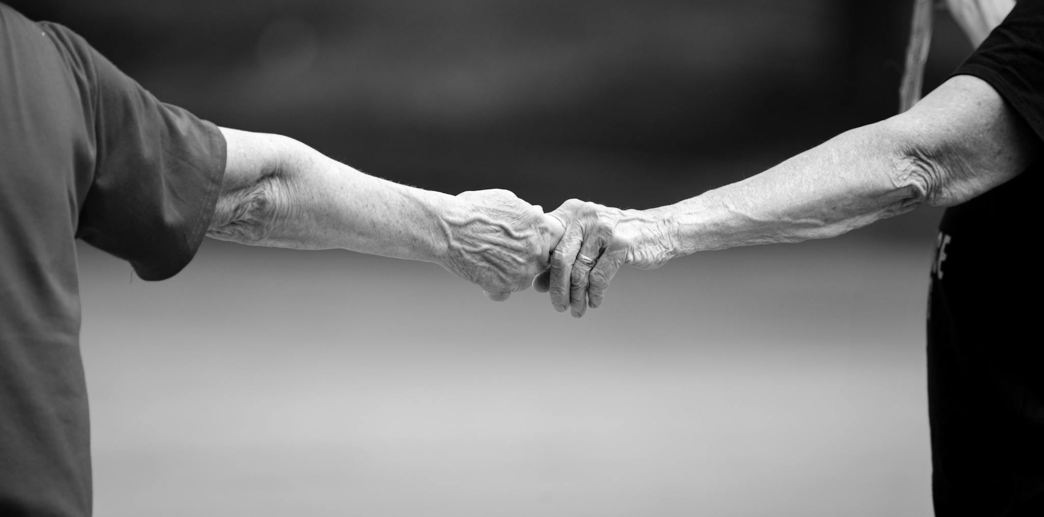 Black and white photo of senior adults holding hands, symbolizing connection and love.