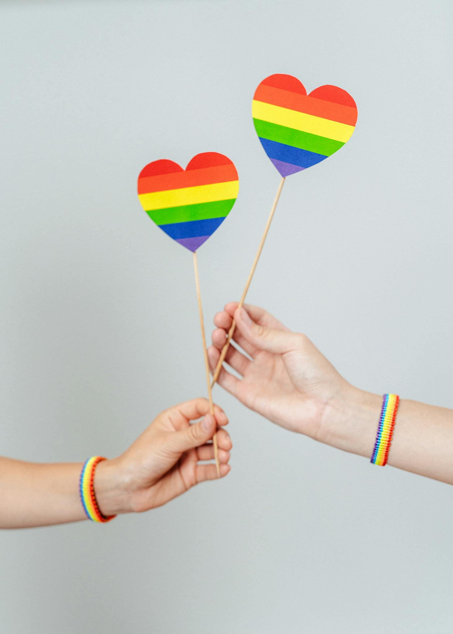Two hands holding rainbow heart symbols, representing love and equality.